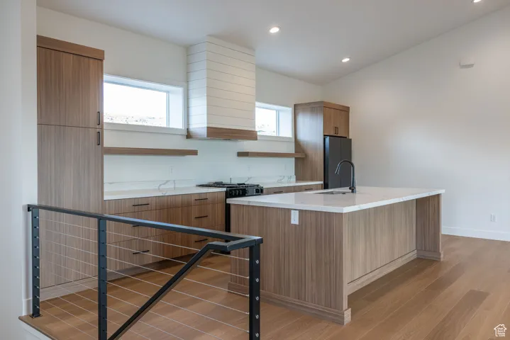 Kitchen featuring open shelves, light wood-type flooring, recessed lighting, an island with sink, and freestanding refrigerator