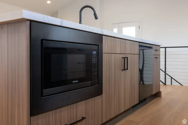 Detailed view of black microwave, modern cabinets, light wood-style floors, stainless steel dishwasher, and recessed lighting