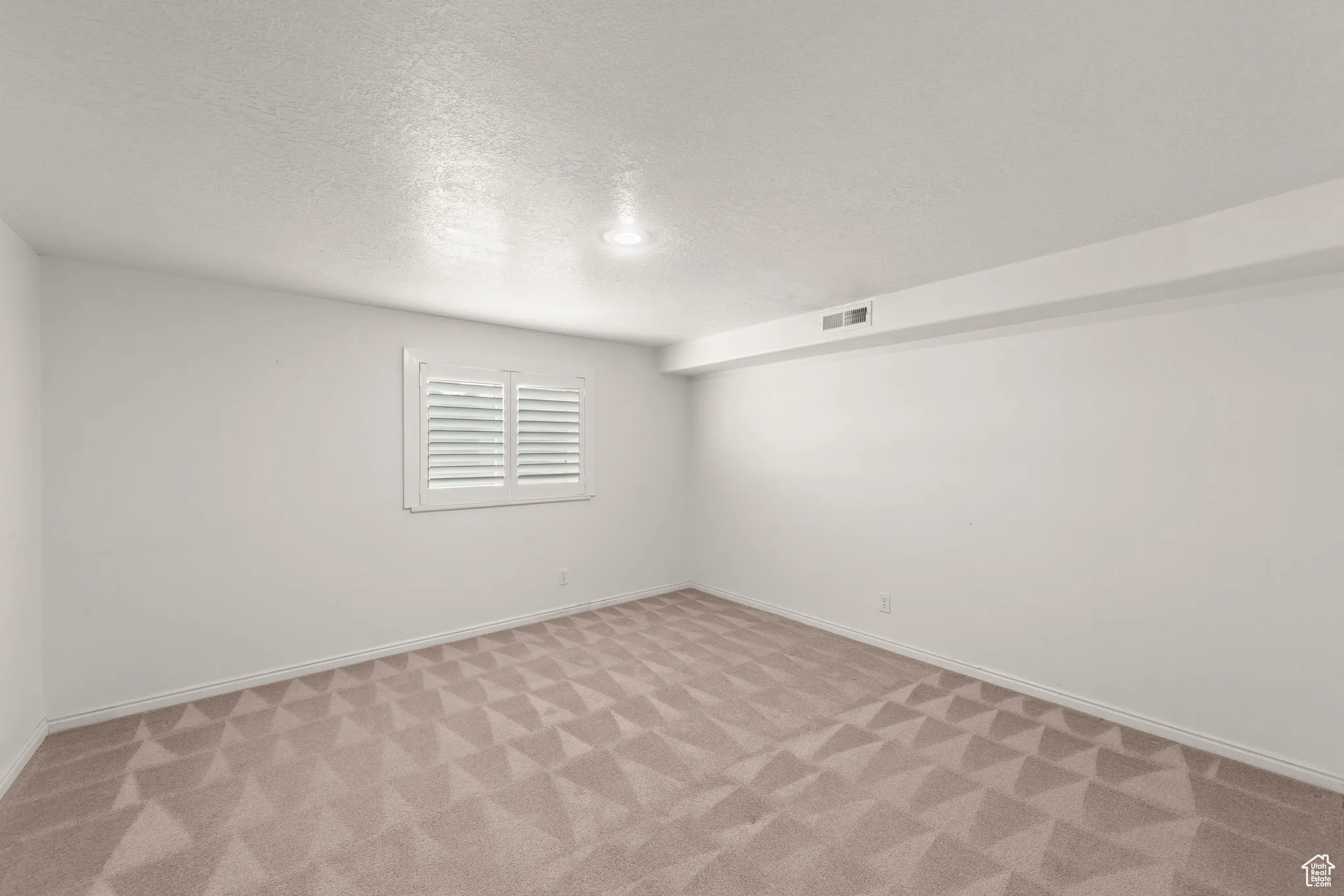 Empty room with a textured ceiling and light colored carpet