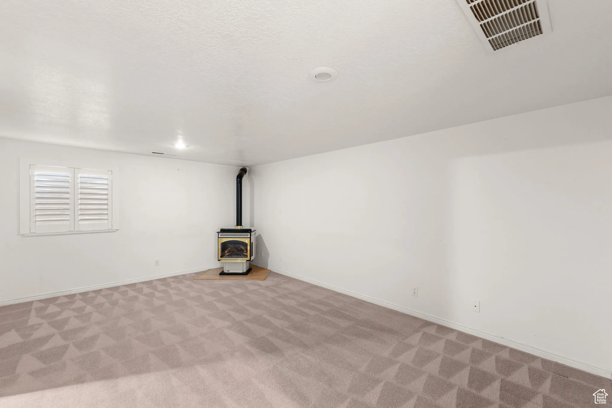 Basement with a wood stove, a textured ceiling, and carpet floors