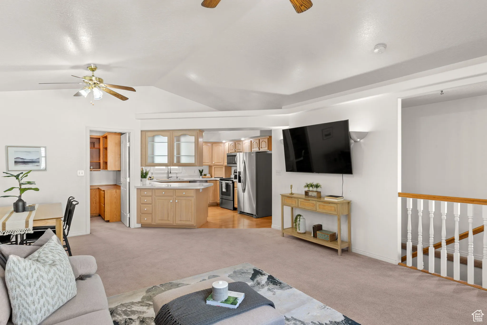 Living area featuring light colored carpet, ceiling fan, and vaulted ceiling