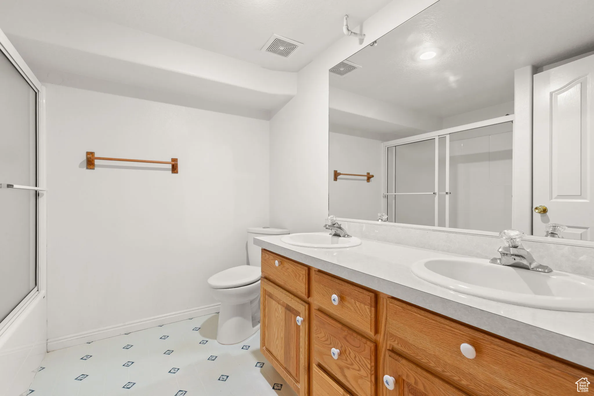 Bathroom featuring double vanity and bath / shower combo with glass door