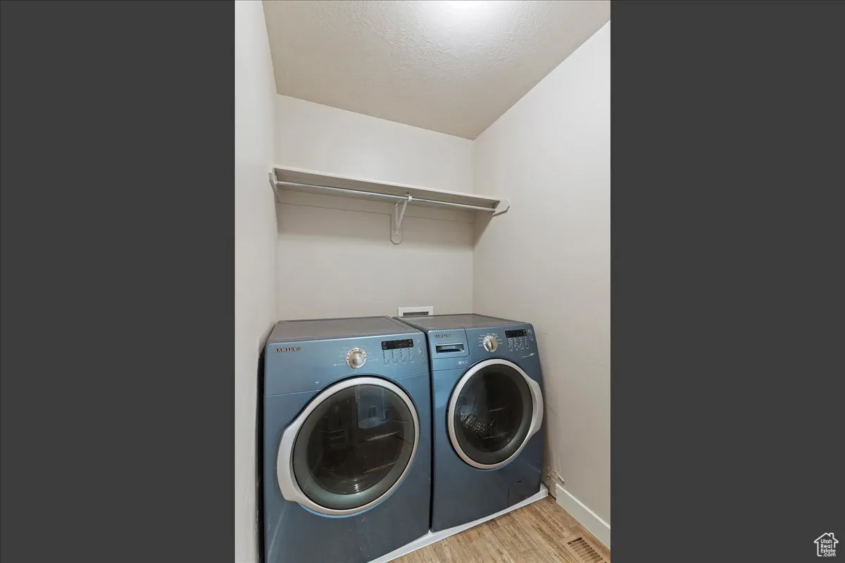 Laundry area featuring light wood-type flooring, a textured ceiling, and washer and dryer