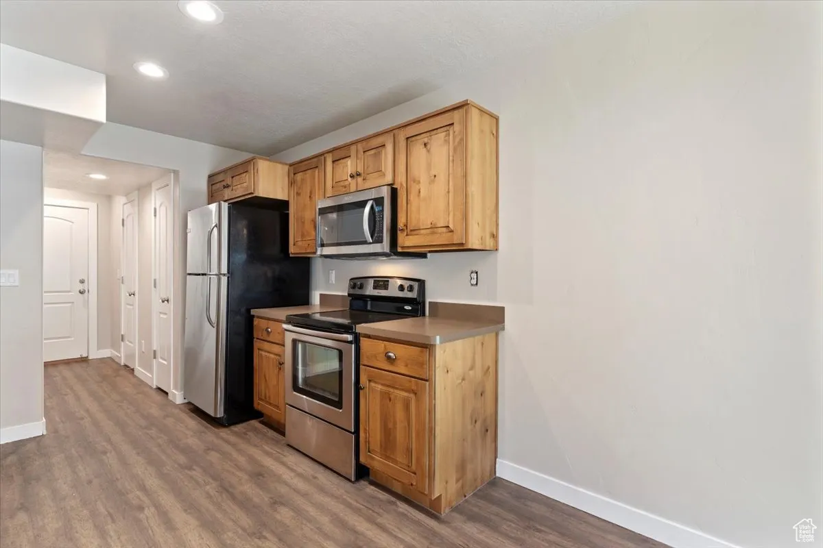 Kitchen with appliances with stainless steel finishes, dark wood-type flooring, recessed lighting, and dark countertops