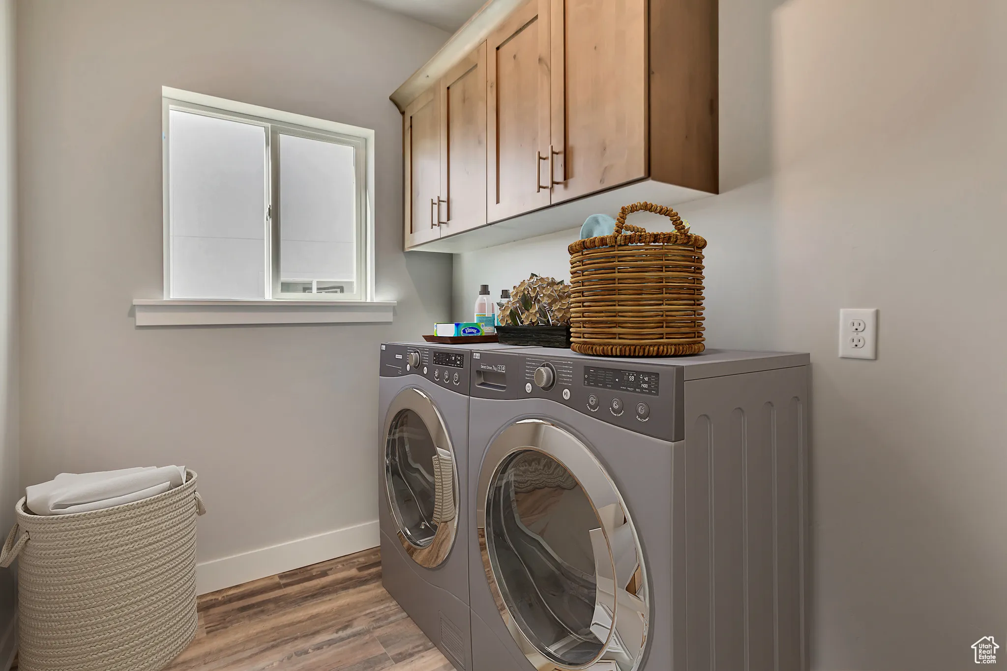 Washroom featuring light wood-style flooring, washer and clothes dryer, and cabinet space