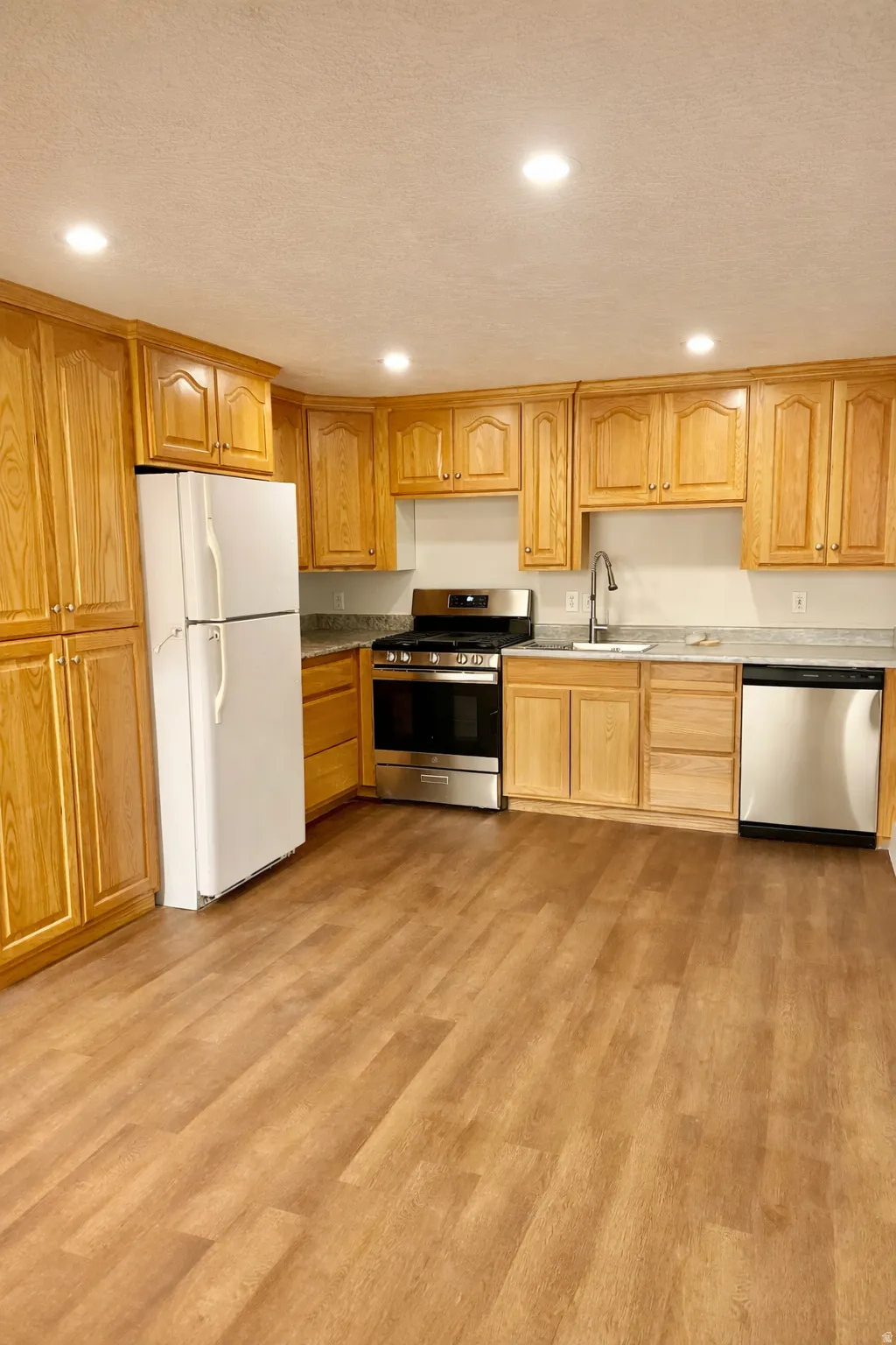 Kitchen with stainless steel appliances, light wood-type flooring, a textured ceiling, recessed lighting, and light stone counters