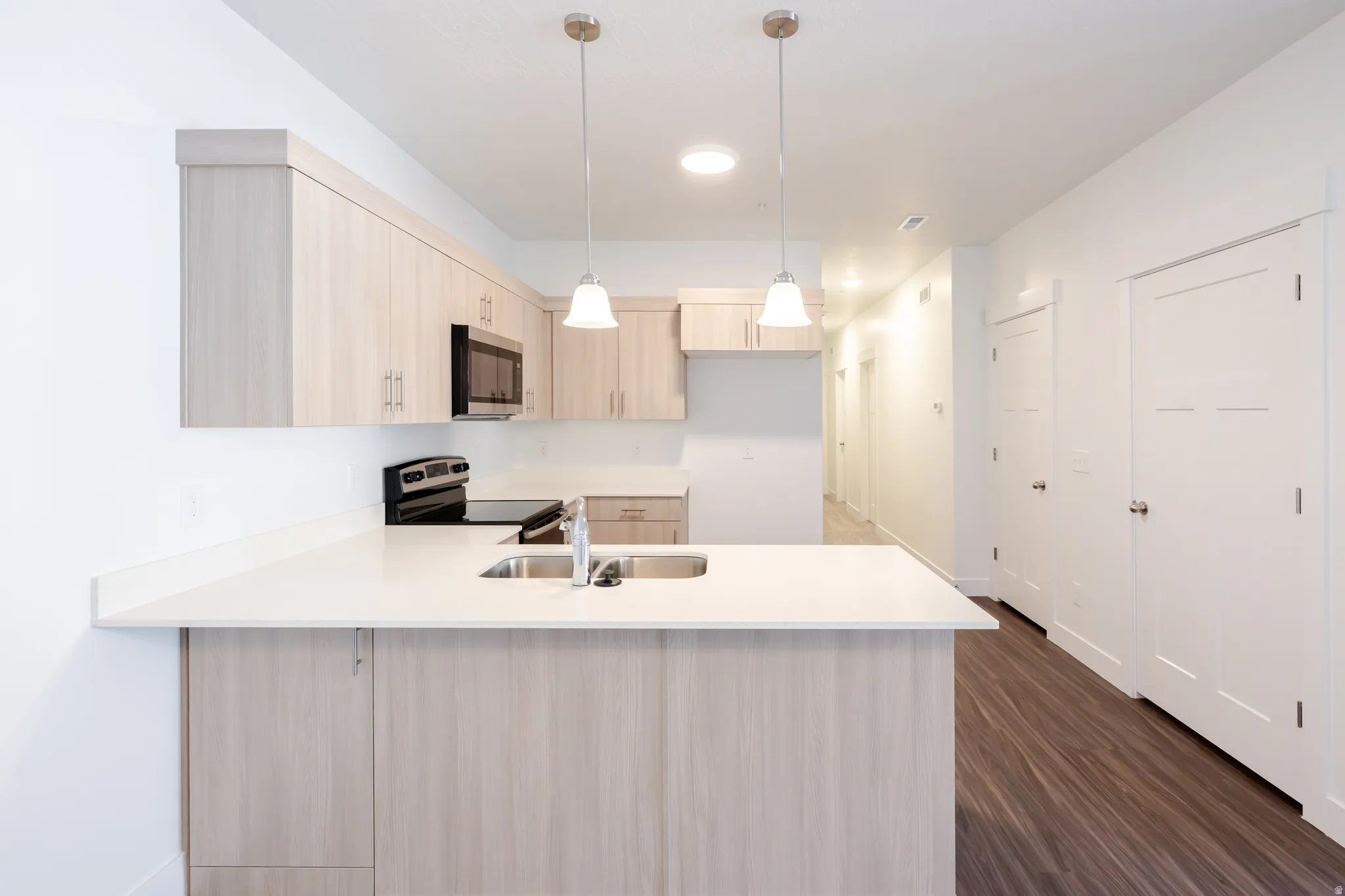 Kitchen featuring light wood finish cabinets, decorative light fixtures, a peninsula, stainless steel appliances, and dark wood-style floors