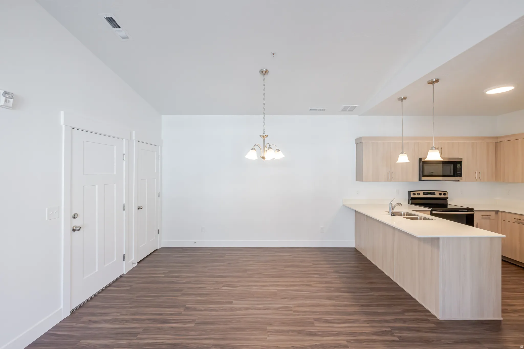 Kitchen with a peninsula, light wood finish cabinetry, stainless steel appliances, dark wood finished floors, and hanging lights