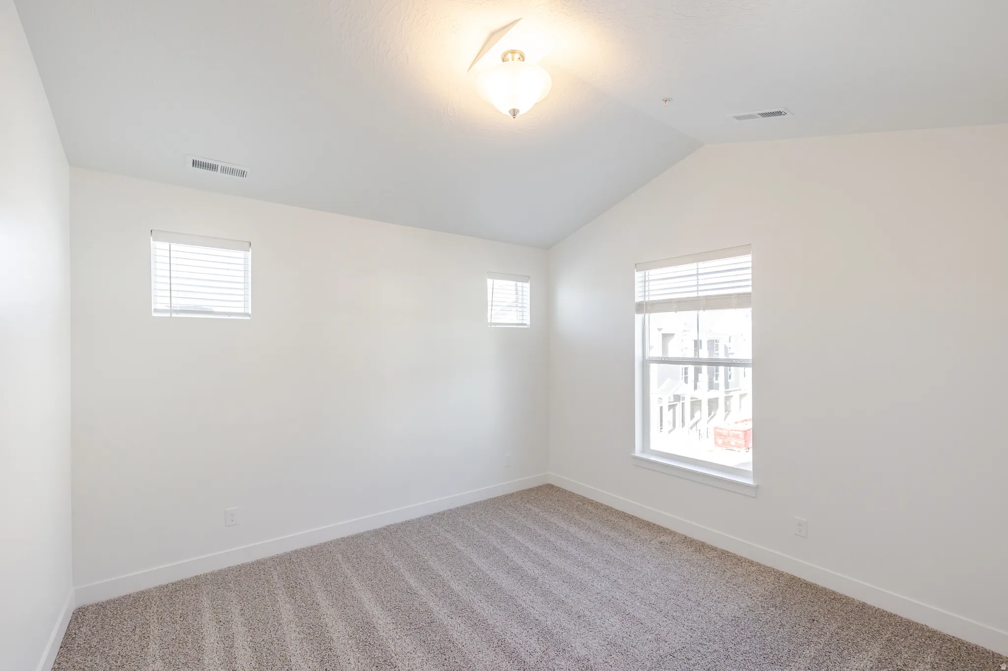 Spare room featuring vaulted ceiling, light colored carpet, and plenty of natural light