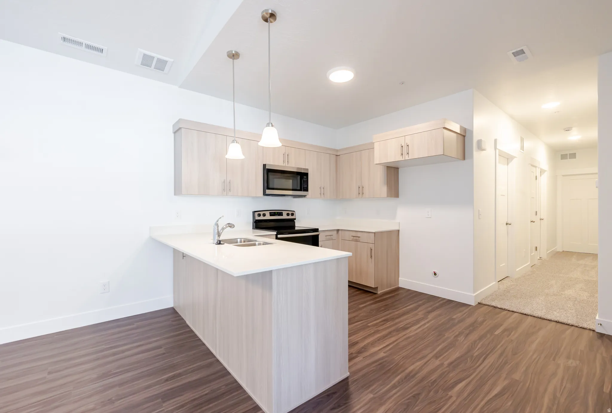Kitchen with a peninsula, light wood finish cabinets, stainless steel appliances, and dark wood-style floors