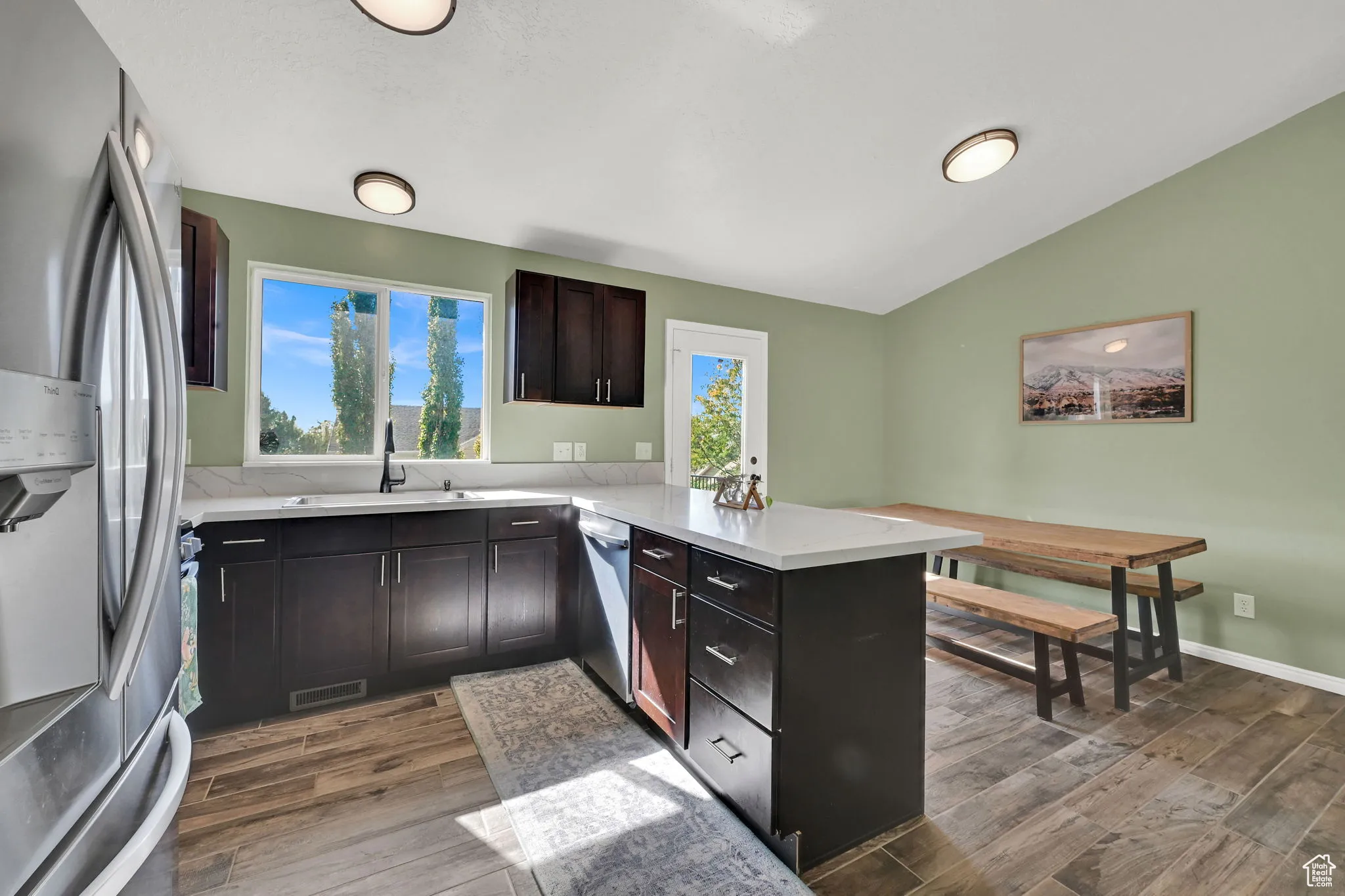 Kitchen featuring a peninsula, stainless steel appliances, dark wood-style floors, lofted ceiling, and dark brown cabinets