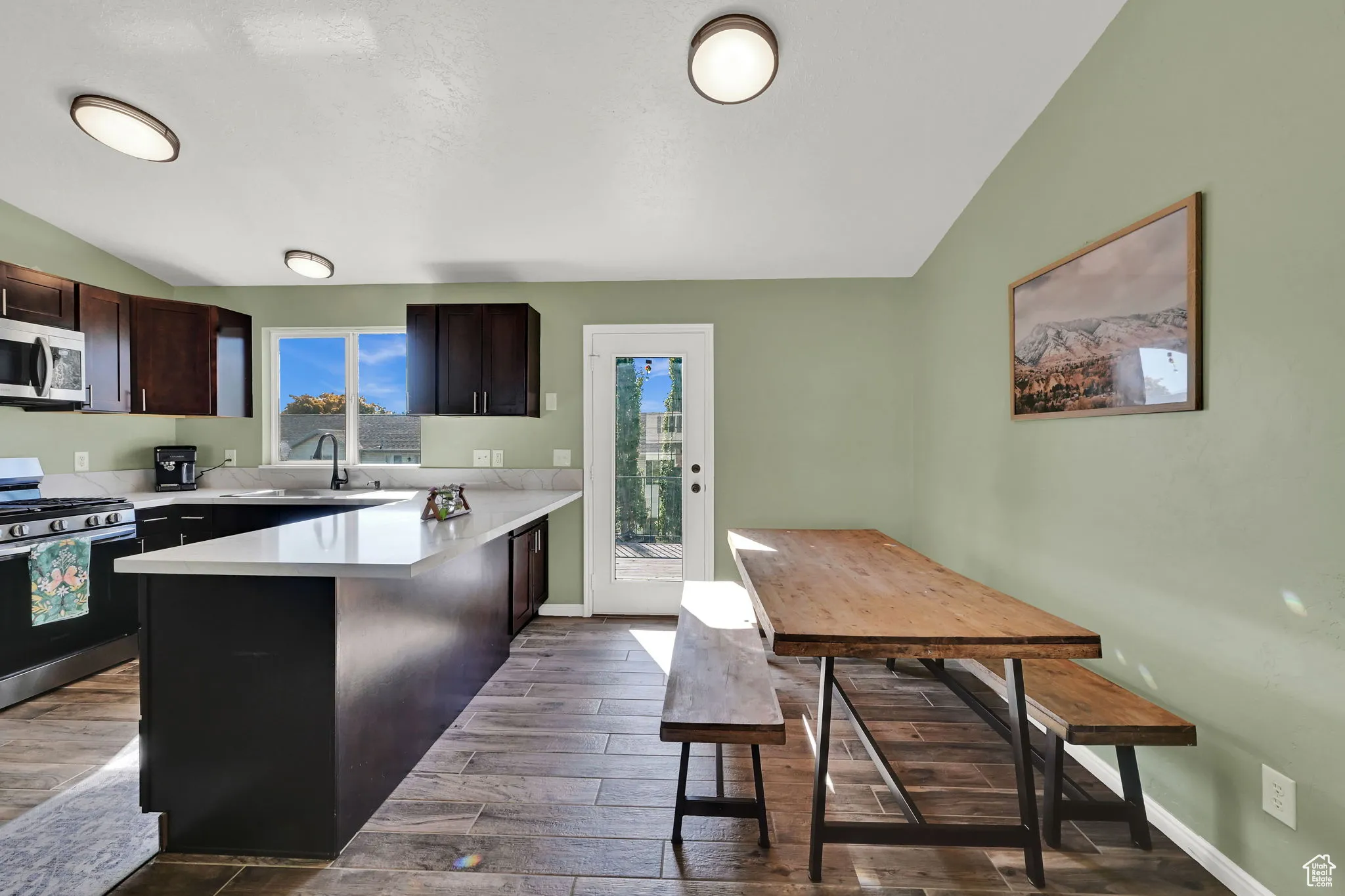 Kitchen featuring vaulted ceiling, appliances with stainless steel finishes, dark wood-style floors, a peninsula, and dark brown cabinets