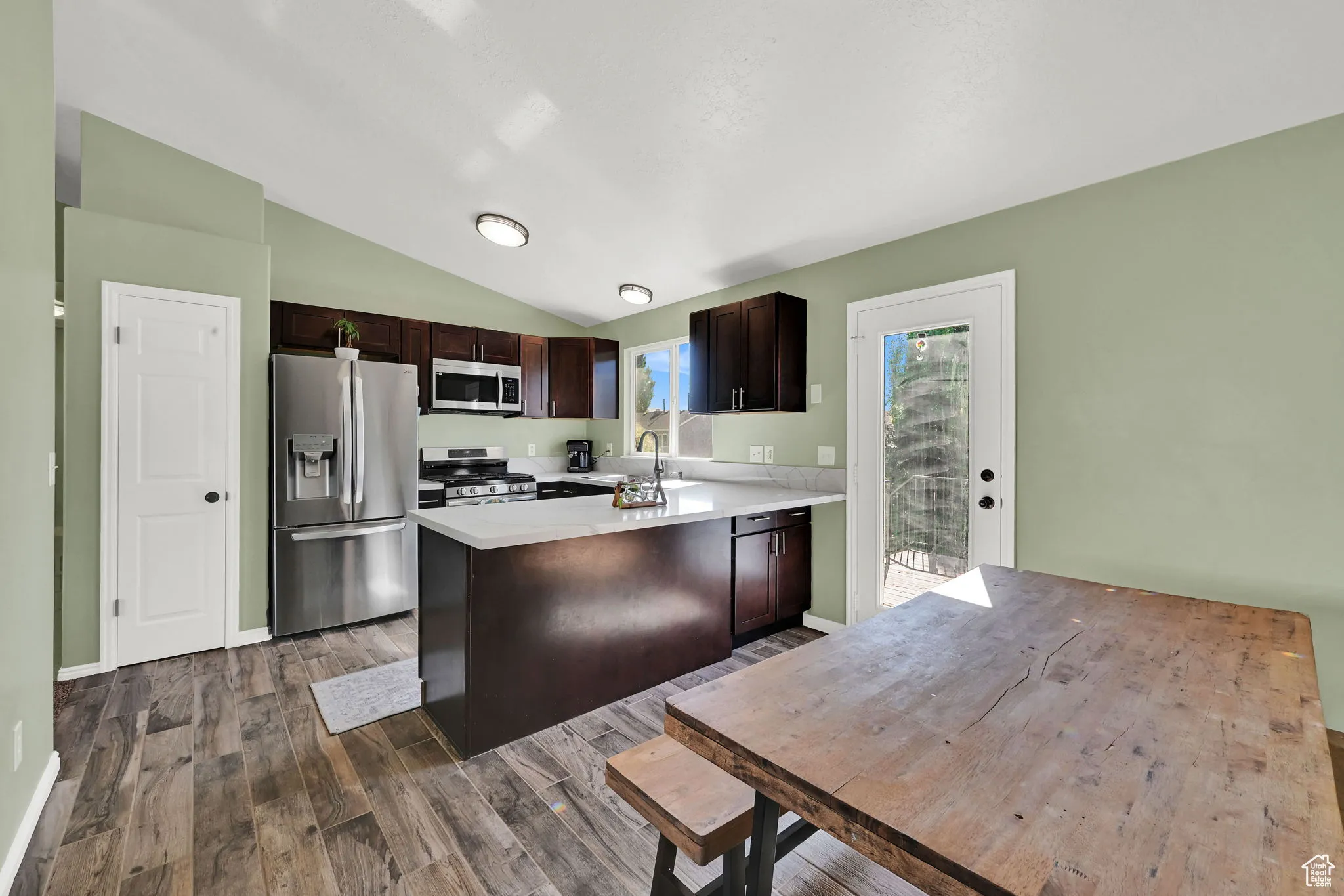 Kitchen featuring dark brown cabinetry, stainless steel appliances, a peninsula, lofted ceiling, and dark wood-type flooring