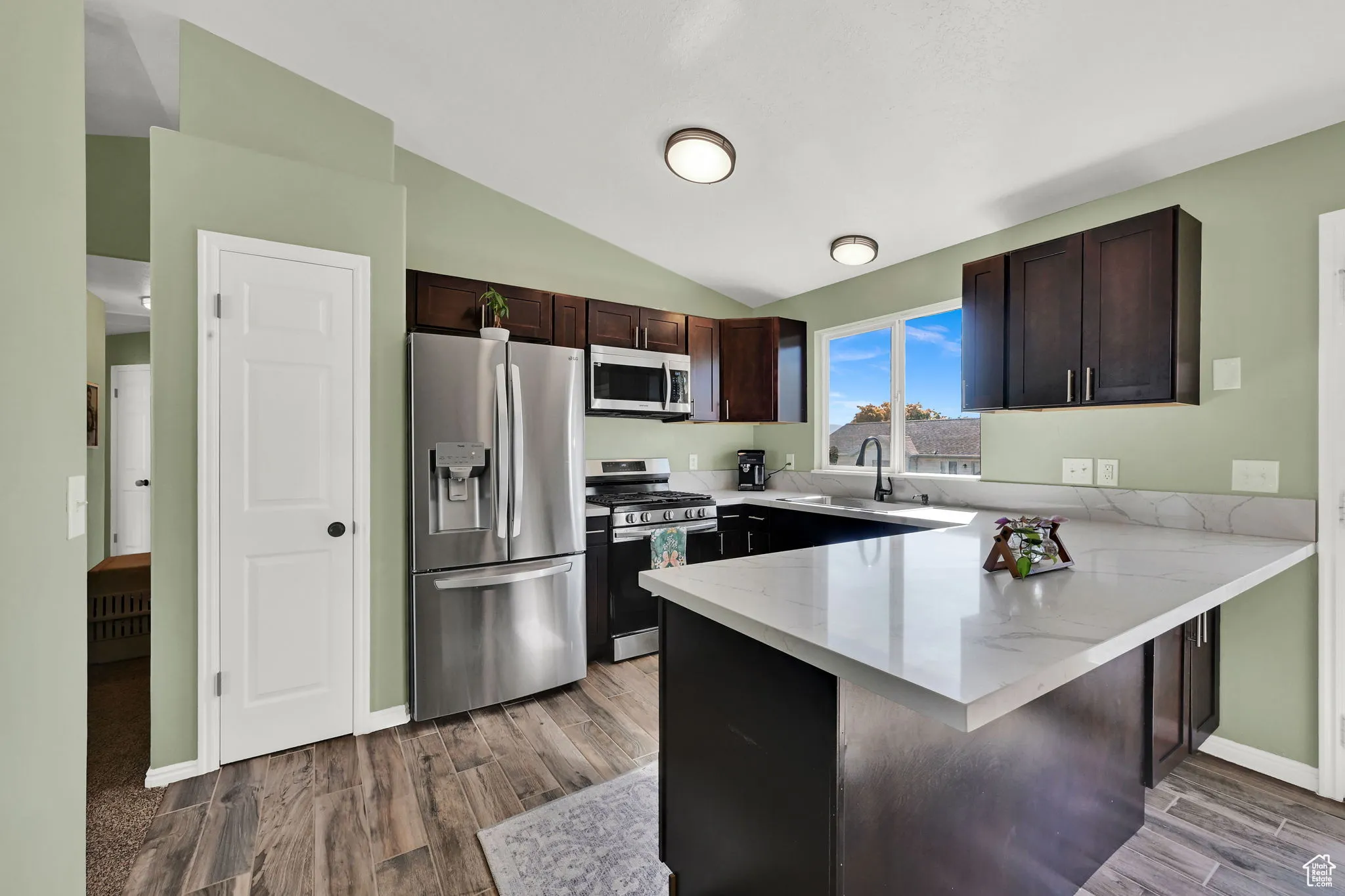 Kitchen with dark brown cabinetry, stainless steel appliances, a peninsula, lofted ceiling, and wood finished floors