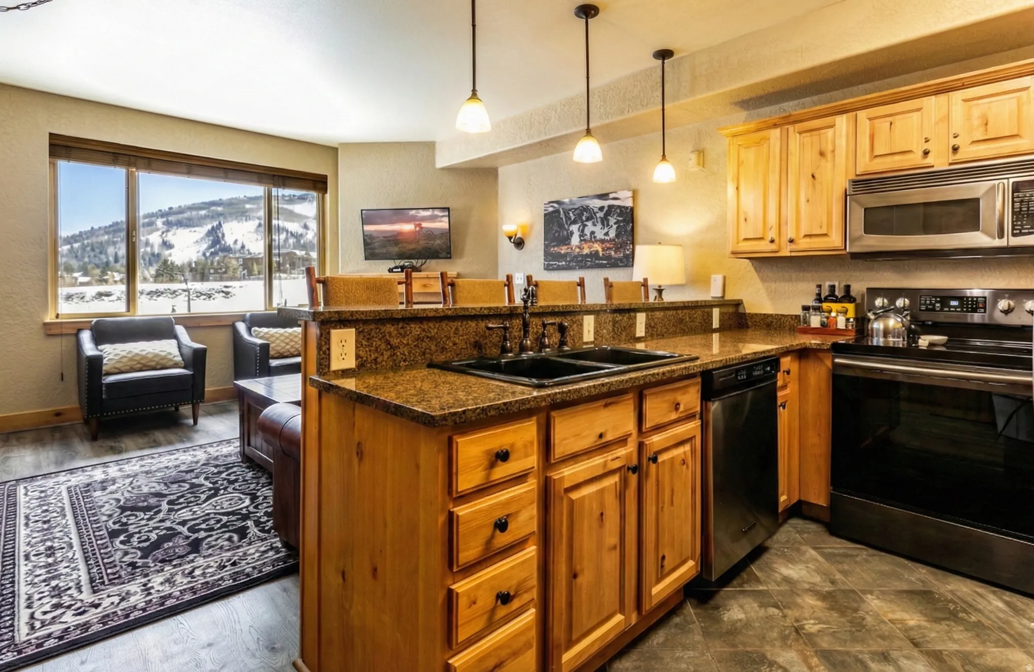 Kitchen featuring stainless steel appliances, hanging light fixtures, dark stone counters, a peninsula, and a textured wall