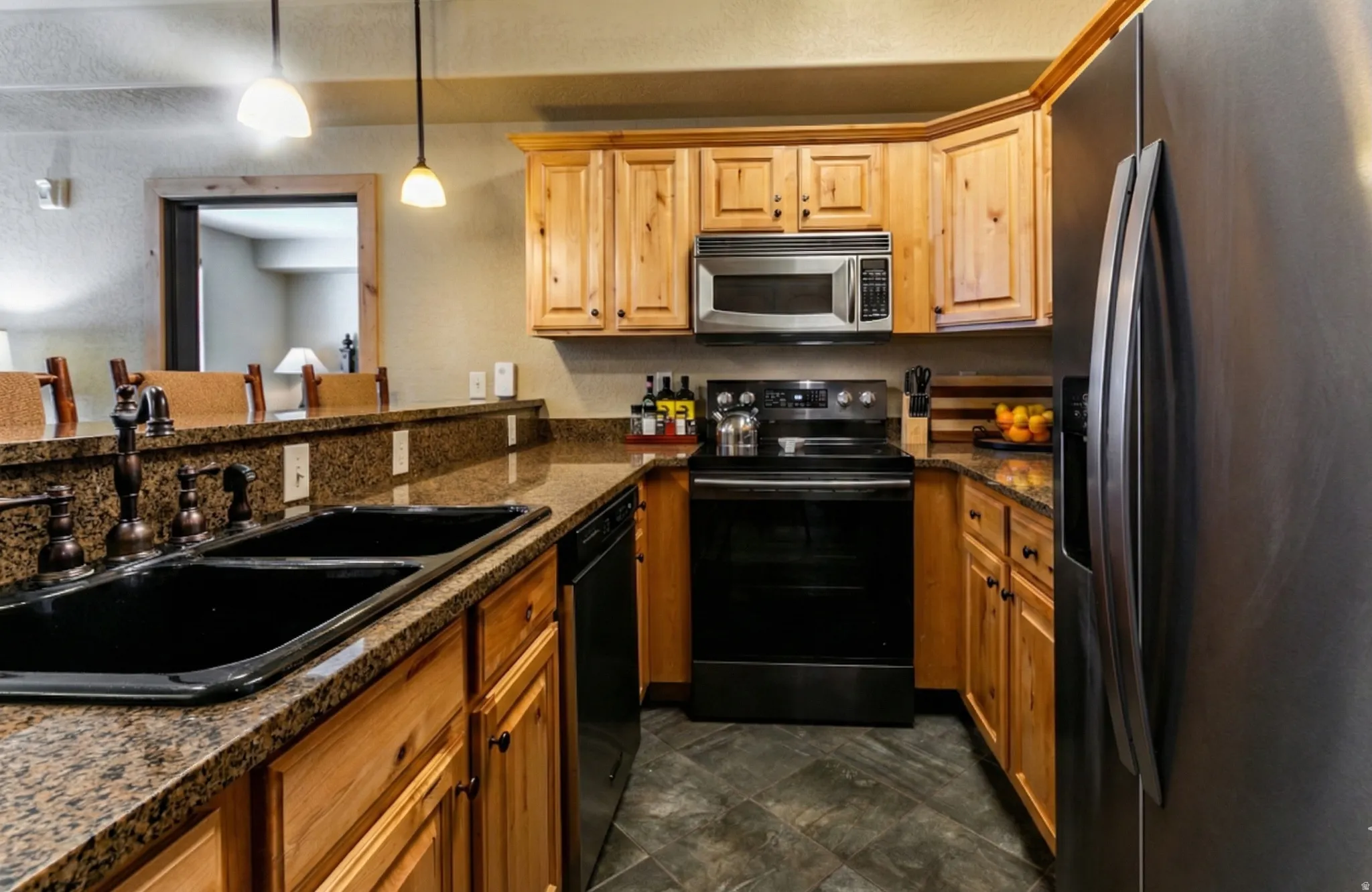Kitchen featuring black appliances, pendant lighting, and dark stone countertops