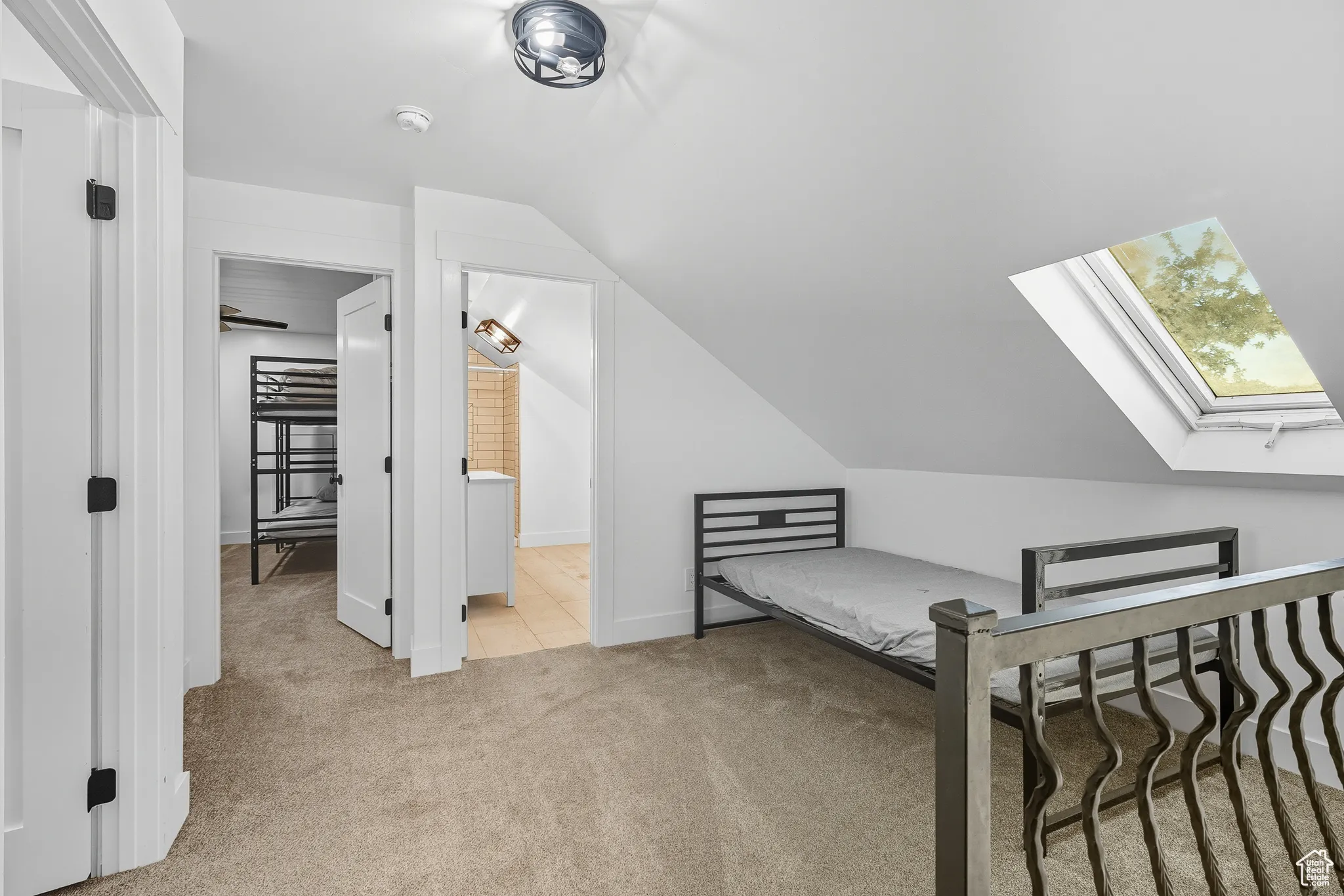 Bedroom with light colored carpet, a skylight, vaulted ceiling, a spacious closet, and connected bathroom