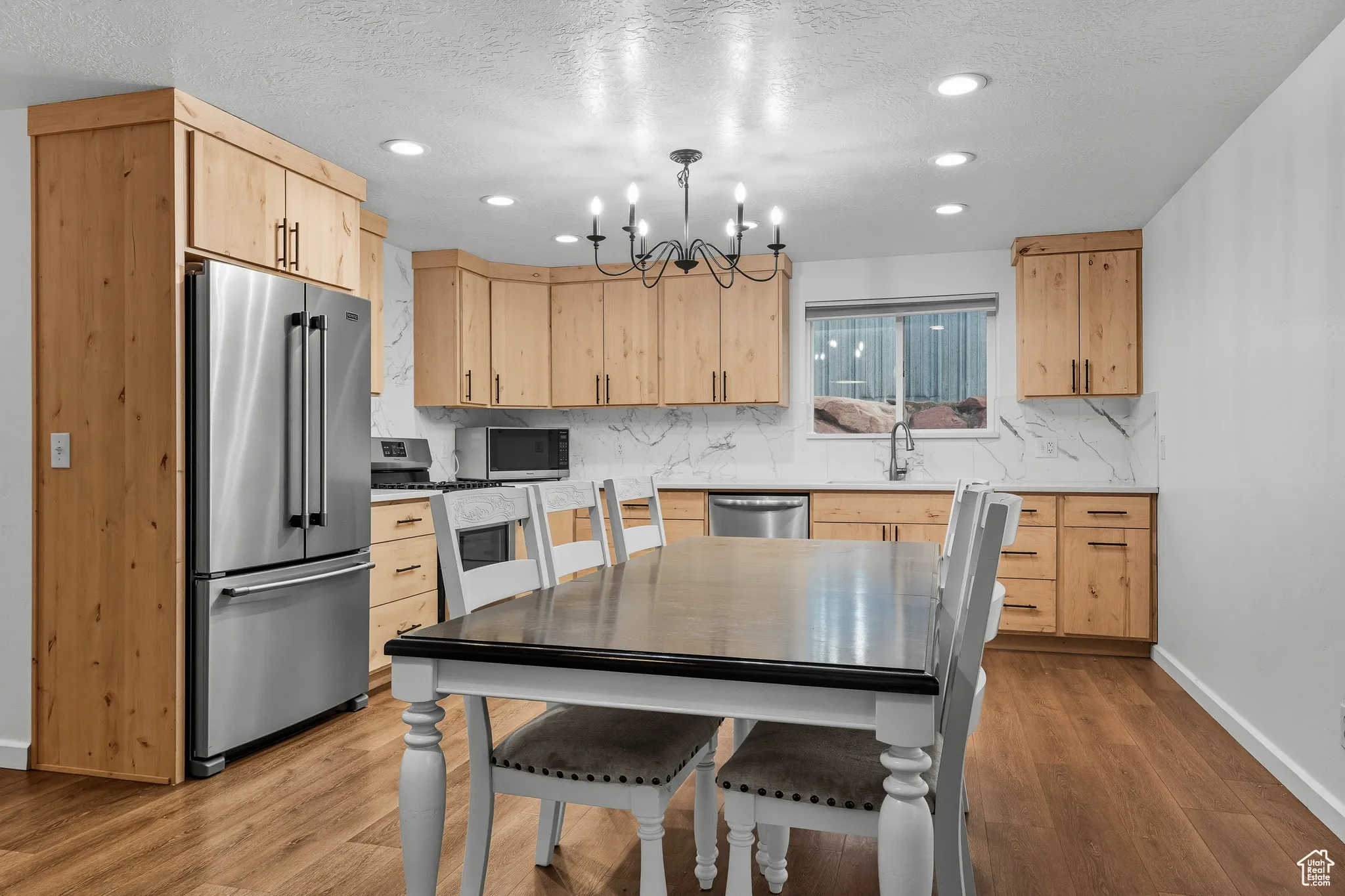 Kitchen with light brown cabinetry, stainless steel appliances, a textured ceiling, pendant lighting, and light stone countertops