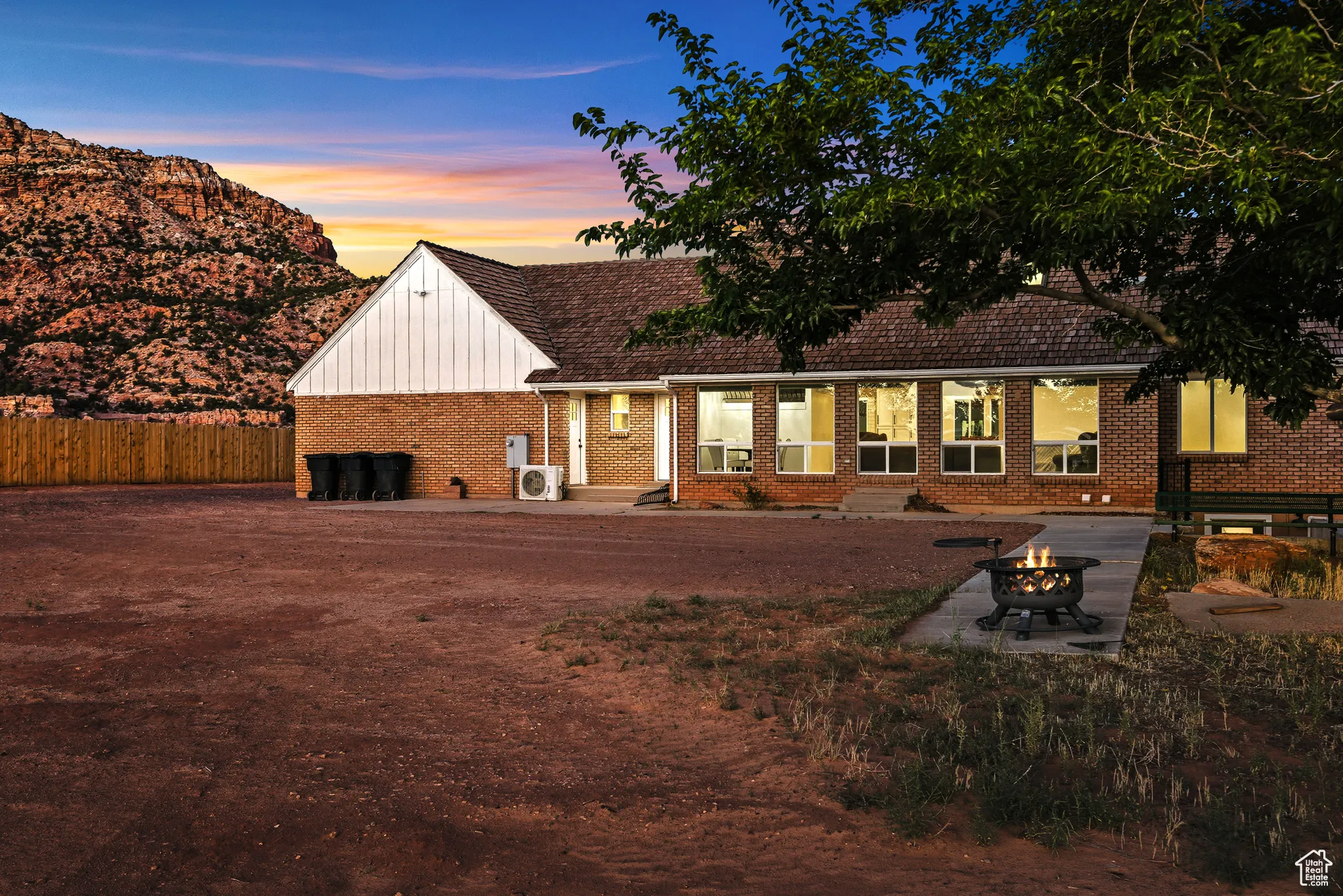 Back of property at dusk featuring a patio area, a fire pit, brick siding, and board and batten siding