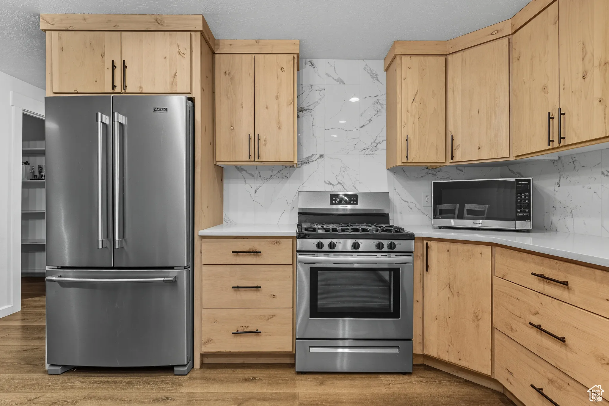 Kitchen with light brown cabinets, appliances with stainless steel finishes, and backsplash