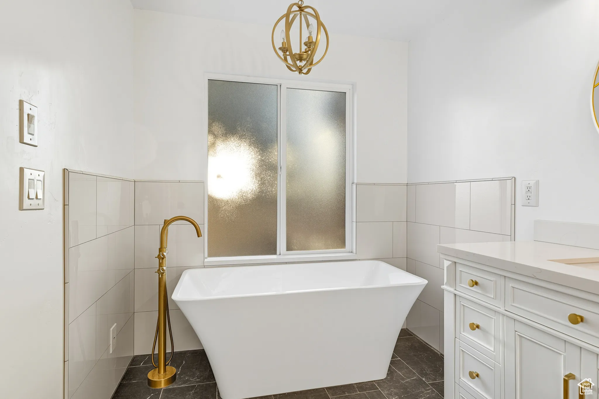 Full bath featuring tile walls, vanity, a freestanding tub, and wainscoting