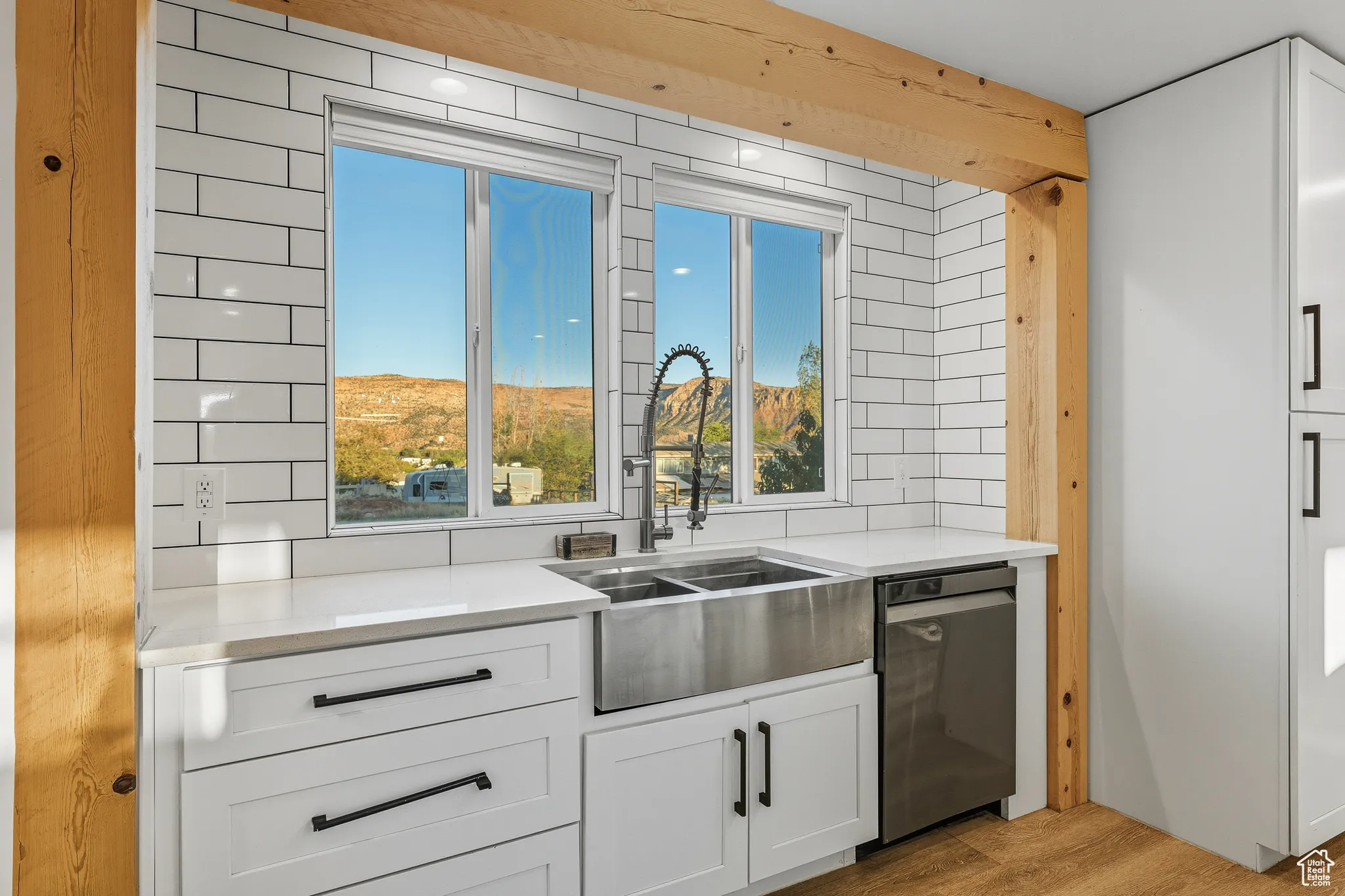 Kitchen featuring white cabinetry, light stone counters, light wood-type flooring, decorative backsplash, and stainless steel dishwasher