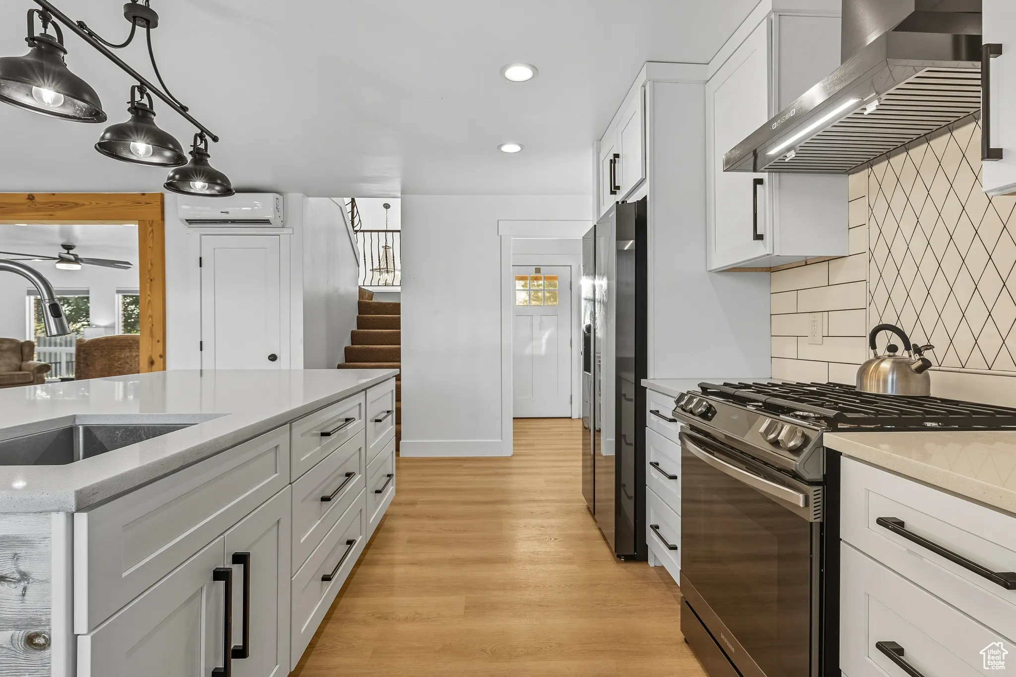 Kitchen with white cabinets, stainless steel appliances, wall chimney exhaust hood, pendant lighting, and light stone counters