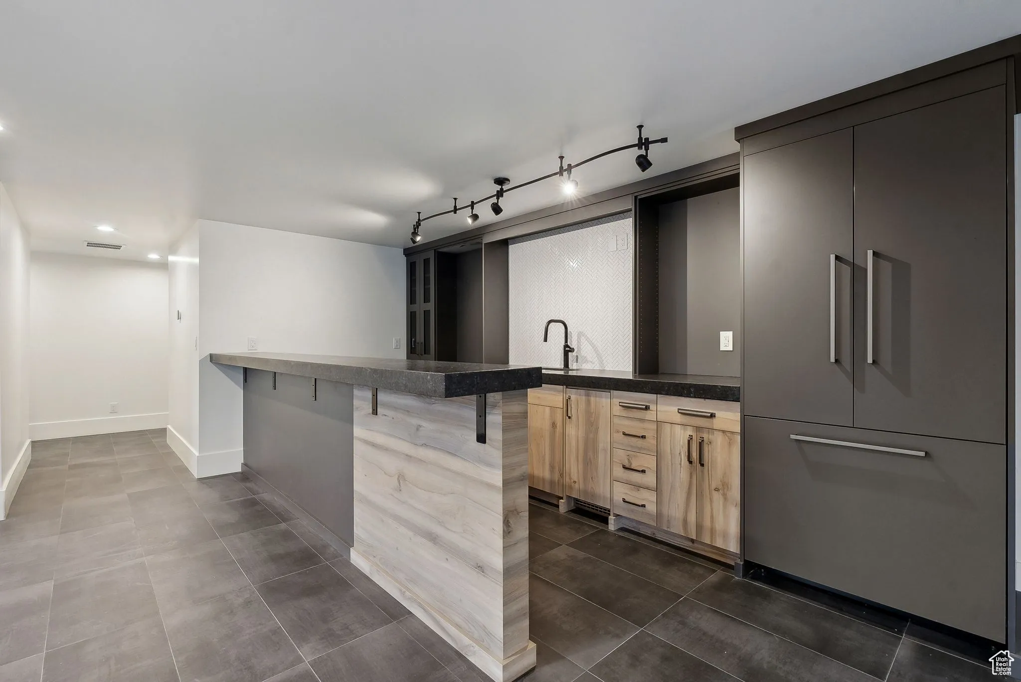 Kitchen with a kitchen breakfast bar, a peninsula, light brown cabinets, dark tile patterned flooring, and modern cabinets