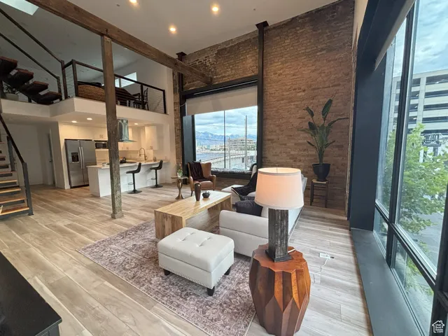Living room,  featuring a high ceiling, stairway, and recessed lighting and exposed brick.