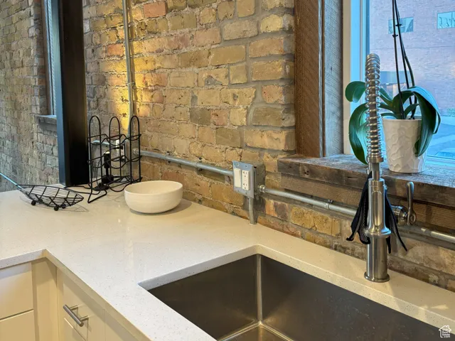 Kitchen featuring light stone countertops, white cabinetry, and brick wall