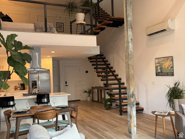 Living room featuring light wood-style flooring, stairs, a towering ceiling, an AC wall unit, and beam ceiling
