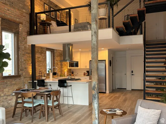 Living room featuring brick wall, a high ceiling, light wood finished floors, and stairs