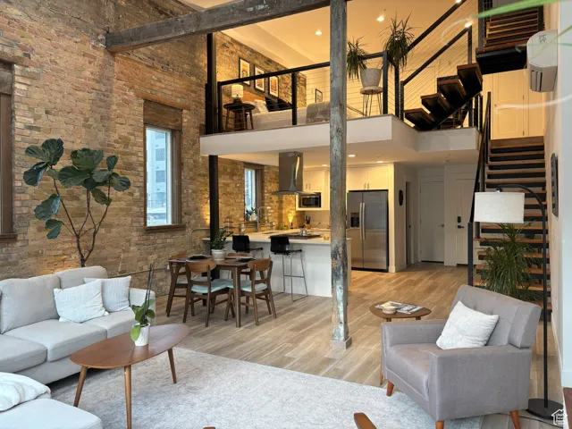 Living room featuring a towering ceiling, light wood finished floors, stairs, and brick wall