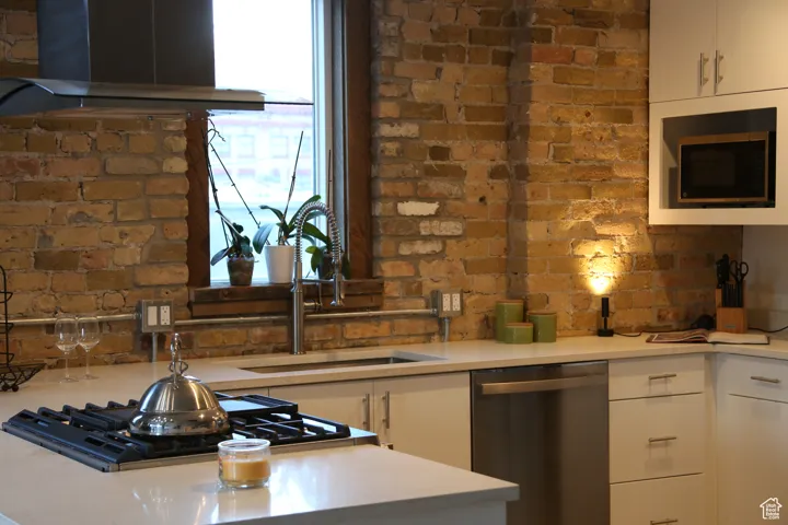 Kitchen with white cabinets, stainless steel appliances, wall chimney exhaust hood, and light stone counters