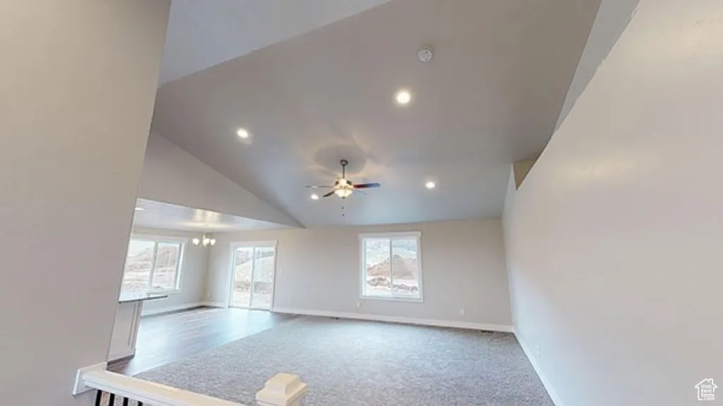 Unfurnished living room with lofted ceiling, a chandelier, light carpet, and recessed lighting
