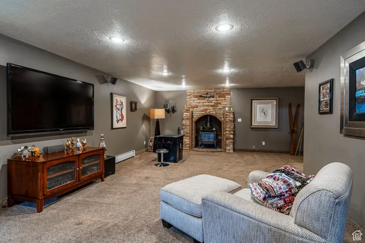 Carpeted living area featuring a textured ceiling, a wood stove, and baseboard heating