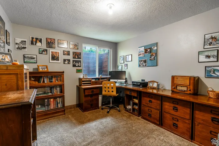 Carpeted office featuring a textured ceiling and baseboards