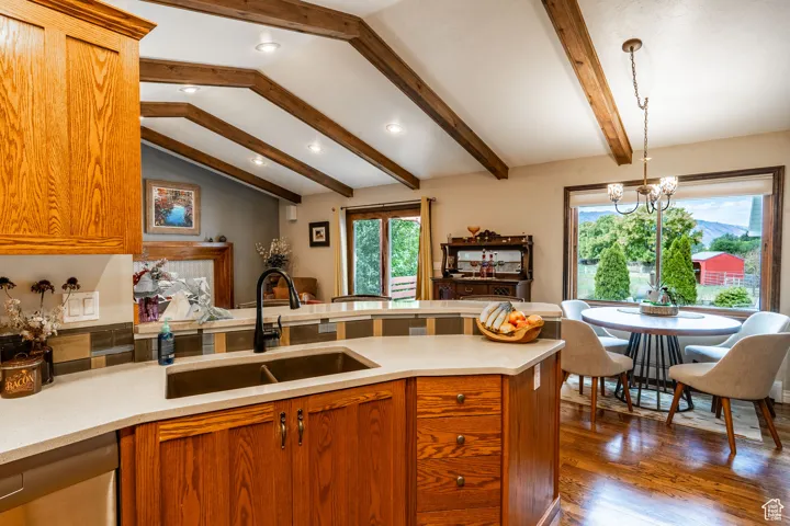 Kitchen featuring brown cabinets, a peninsula, dark wood-style flooring, stainless steel dishwasher, and hanging light fixtures