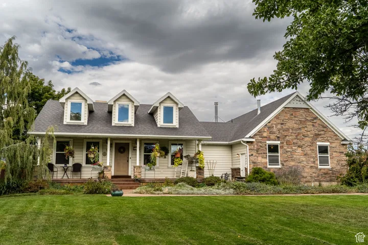 View of front facade featuring roof with shingles, a porch, a front yard, and stone siding