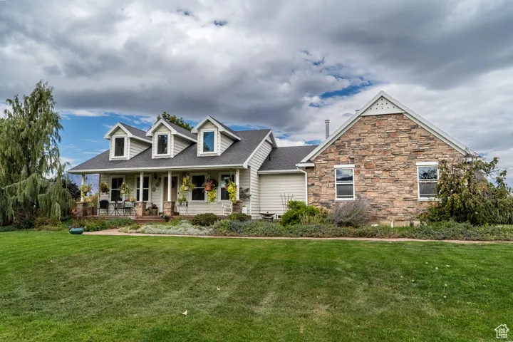 New england style home with covered porch, a front yard, roof with shingles, and stone siding