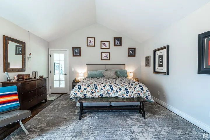 Primary bedroom with lofted ceiling and dark wood-type flooring