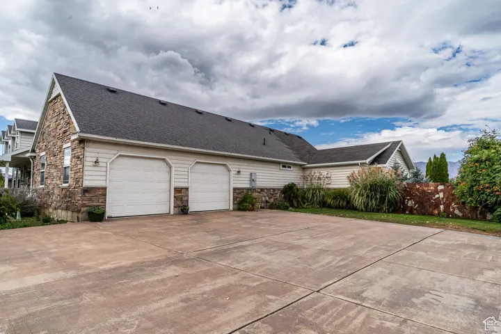 View of property exterior with stone siding, driveway, and a shingled roof