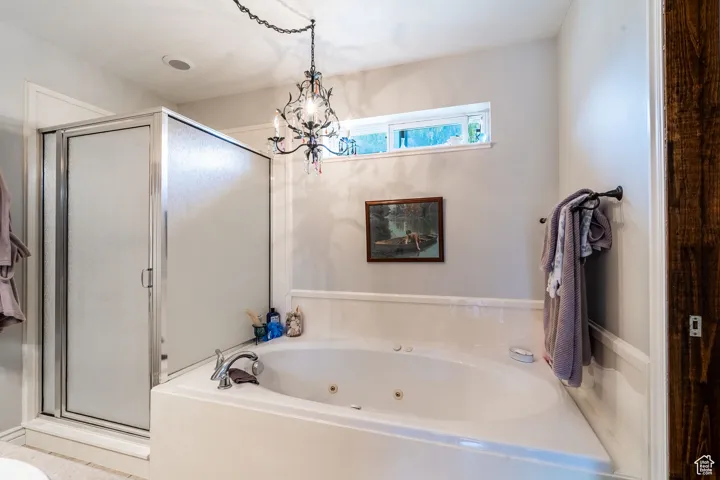 Primary bath featuring a stall shower, a whirlpool tub, and a chandelier