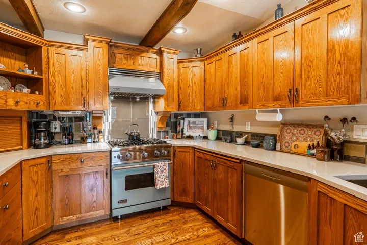 Kitchen featuring stainless steel appliances, light wood finished floors, range hood, beam ceiling, and brown cabinets