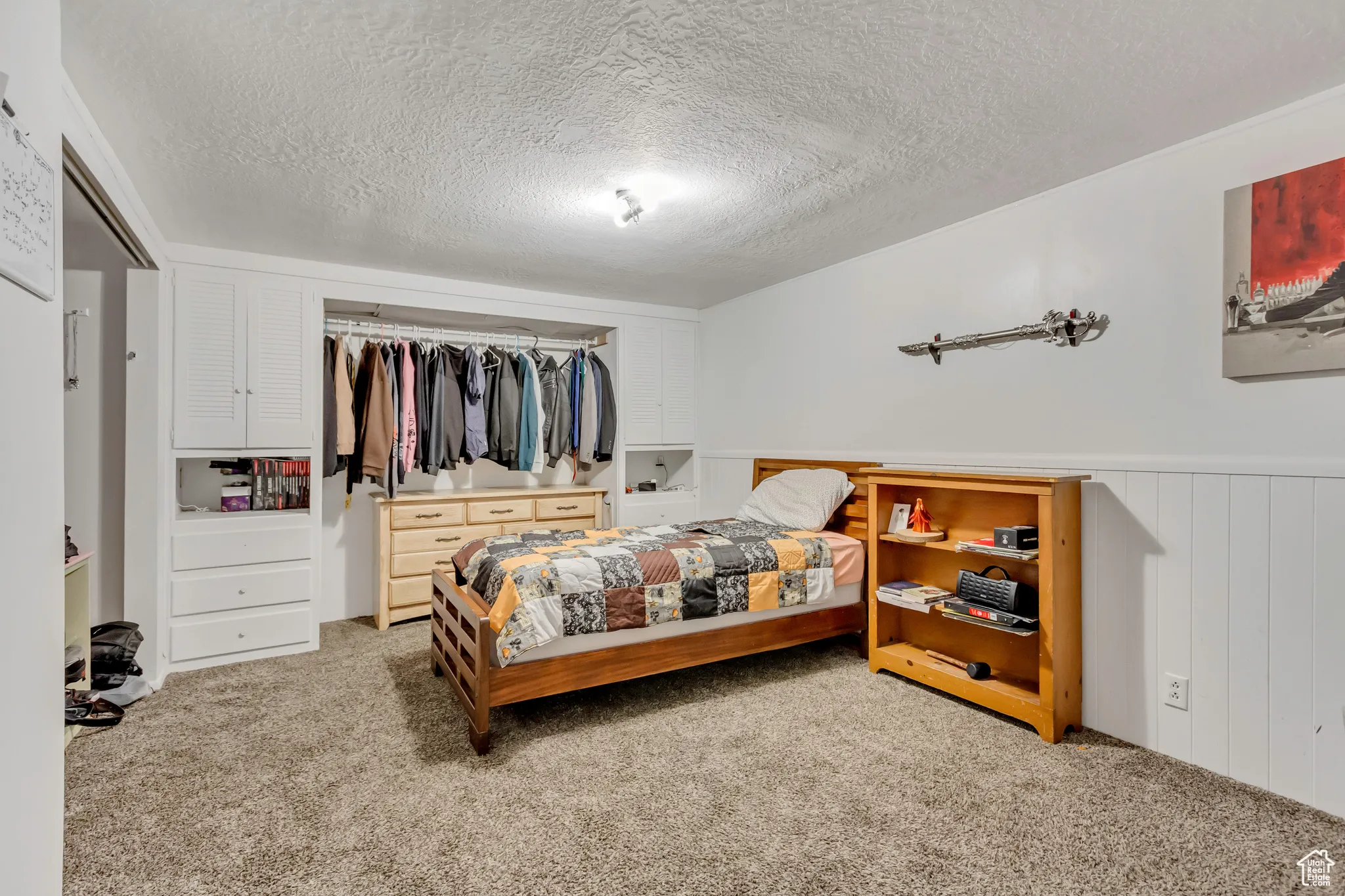 Carpeted bedroom with a closet, a textured ceiling, and a wainscoted wall