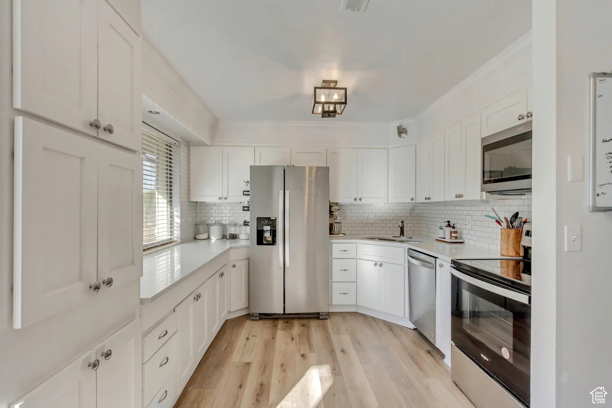 Kitchen featuring appliances with stainless steel finishes, light wood-type flooring, white cabinetry, decorative backsplash, and light stone counters