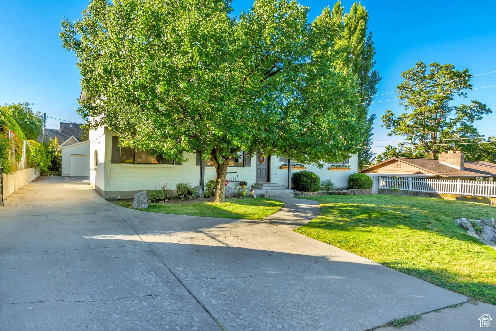View of property hidden behind natural elements with brick siding, a garage, and concrete driveway