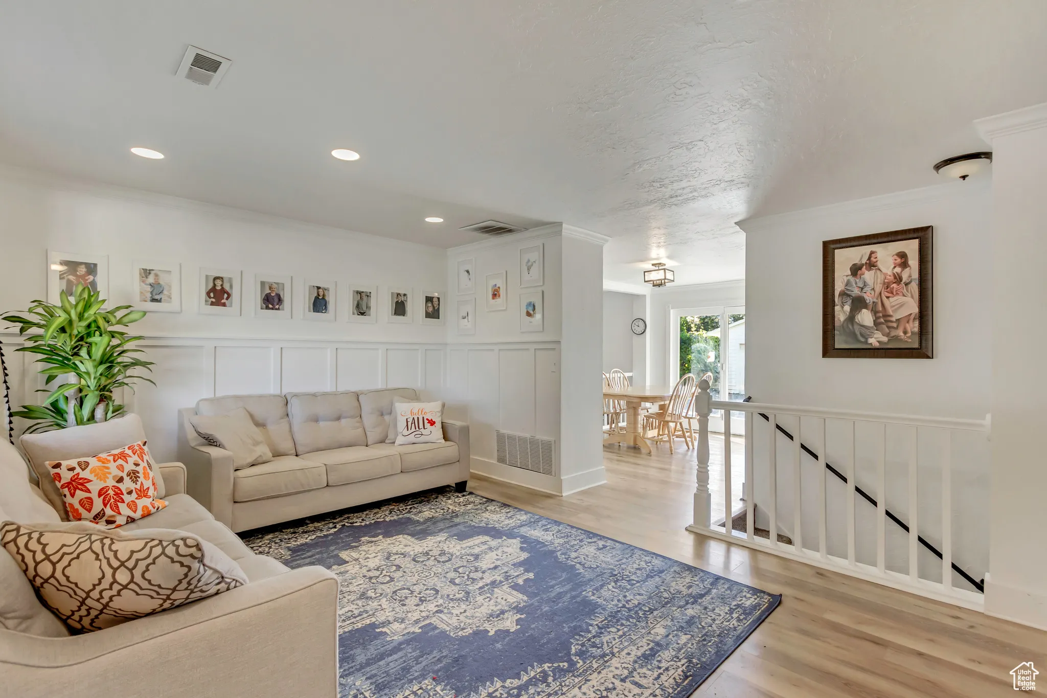 Living room with a decorative wall, light wood-type flooring, ornamental molding, wainscoting, and recessed lighting