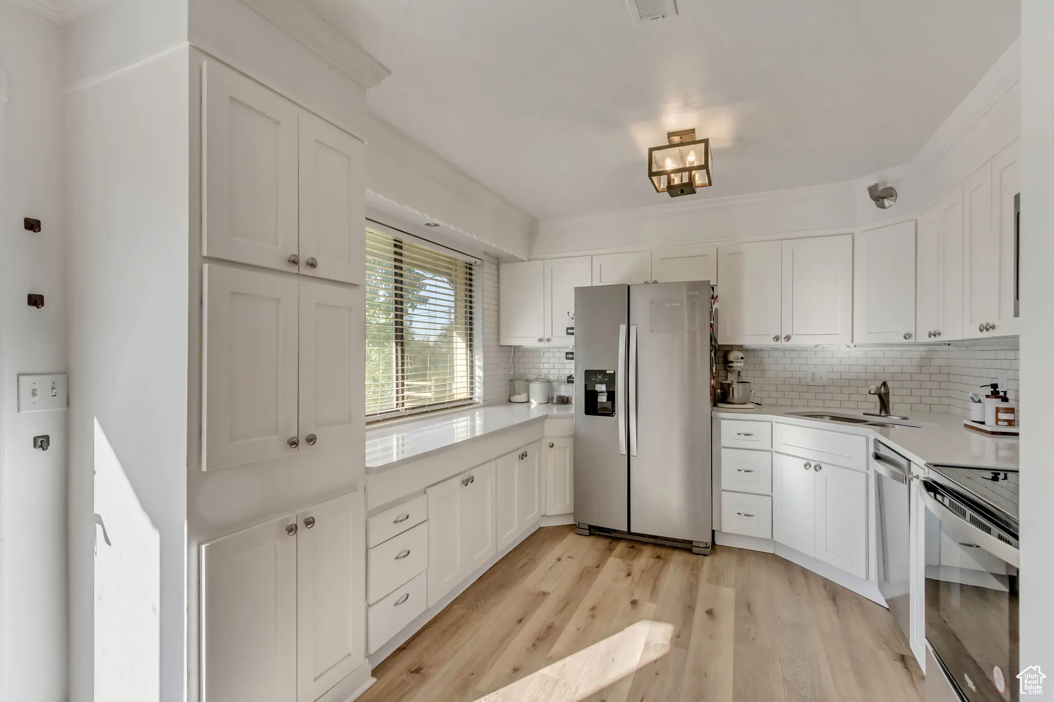 Kitchen featuring appliances with stainless steel finishes, white cabinetry, light wood-style flooring, decorative backsplash, and crown molding