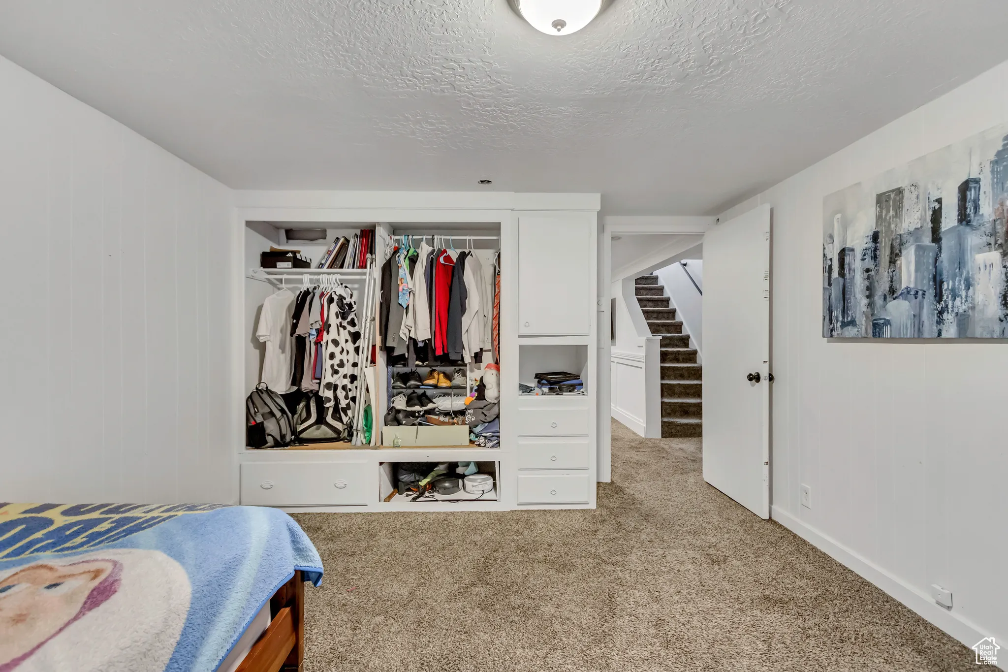 Bedroom with light colored carpet, a textured ceiling, a closet, and wooden walls